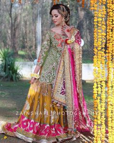 a woman in a green and yellow dress standing under an orange flower covered archway with flowers