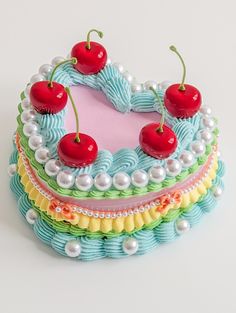 a heart shaped cake with cherries and pearls on the top, sitting on a white surface