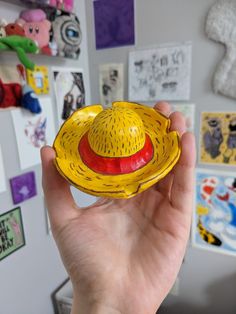 a hand holding a yellow hat in front of a wall with pictures and magnets on it