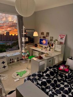 a bedroom with a bed, desk and window overlooking the city at sunset or dawn