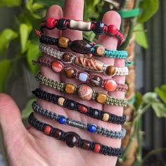 a hand holding several different bracelets on it's palm with a plant in the background