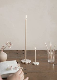 a person sitting at a table reading a book with candles in front of them on the table