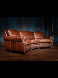 a brown leather couch sitting on top of a wooden floor next to a blue wall