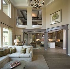 a living room filled with furniture and a chandelier hanging from the top of two story ceilings