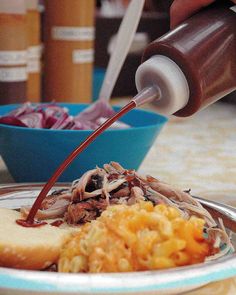 someone is pouring sauce over some food on a plate with bread and coleslaw