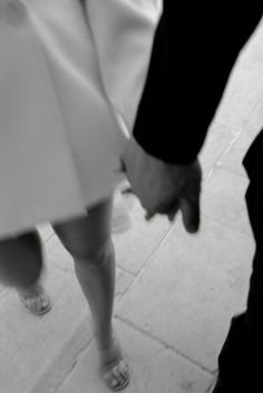 a man and woman holding hands while walking down the street