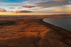 an aerial view of the water and land at sunset, with some clouds in the sky