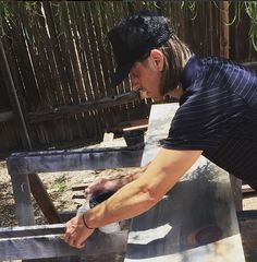 a man in a black shirt and hat working on a piece of wood with a grinder