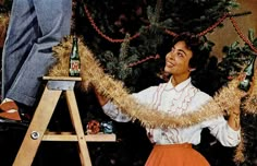 a woman standing next to a ladder with christmas decorations on it's legs and holding onto a man's leg