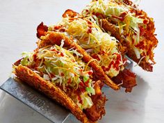 several taco shells with shredded cheese and toppings on them sitting on a metal tray