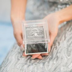 a woman is holding a ring in her hand while sitting on a chair with a clear box