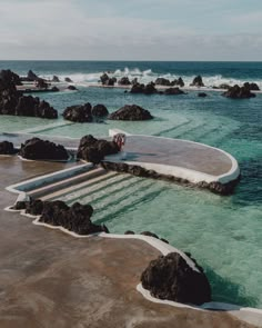 a person standing on some steps in the water next to rocks and oceanweeds