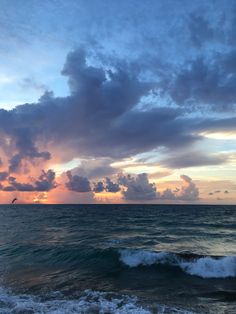 the sun is setting over the ocean with clouds in the sky and waves crashing on the shore