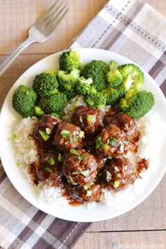 a white plate topped with meatballs and broccoli on top of rice next to a fork