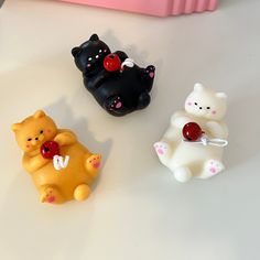 three small toy bears sitting next to each other on a white counter top in front of a pink container