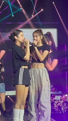 two girls are standing on stage with microphones in their hands and one girl is singing