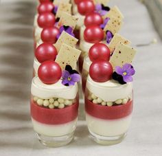 small red and white desserts are arranged in glass containers with purple flowers on them