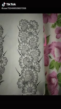 an intricate design on the side of a sheet of paper with pink flowers in the background