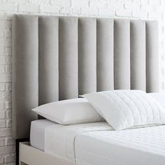 a bed with white sheets and pillows in front of a brick wall that has been made into an upholstered headboard