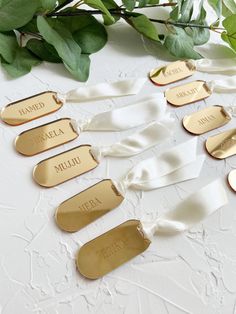 gold name tags with white satin ribbons and greenery in the background on a table