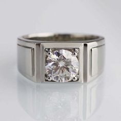 a white gold ring with a square cut diamond in the center, on a reflective surface