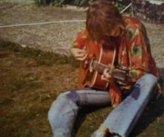 a man sitting on the ground playing an acoustic guitar