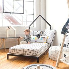 a little boy sitting on top of a bed next to a table and chair in a room