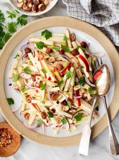 a white plate topped with sliced apples and onions next to a bowl filled with nuts