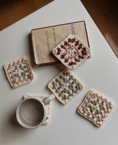 four crocheted coasters and a coffee cup on a table with a book