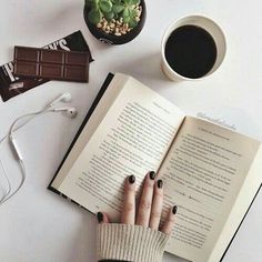 a woman reading a book next to a cup of coffee