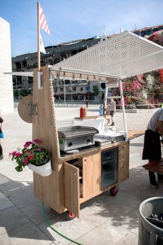 an outdoor bbq grill with potted plants on the side and people standing around