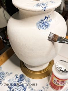 a white vase sitting on top of a table next to a paint can and brush