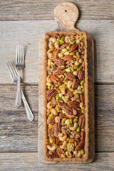 a pie with nuts and pistachios in it on a wooden table next to a fork