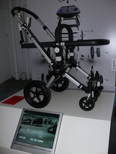 a wheel chair on display in front of a white board with black wheels and an electronic device next to it