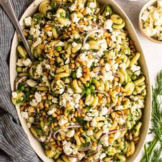 a white bowl filled with pasta salad and topped with feta cheese, onions, green beans