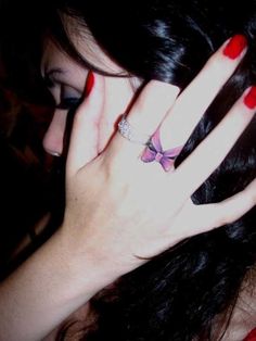 a woman with long black hair and red nails holding her hand up to her face