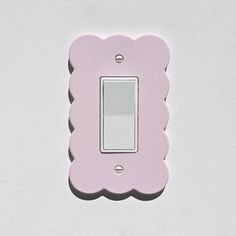 a pink light switch cover with scalloped edges on a white wall in the shape of a flower