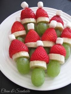 some grapes and strawberries in santa hats are on a white plate with green grapes