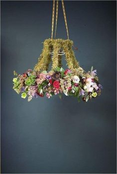 a flower arrangement hanging from a chandelier with moss and flowers in the center