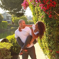 a man carrying a woman on his back as they walk down a sidewalk next to flowers