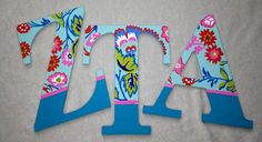 the letters are decorated with colorful flowers and blue paint on white paper, along with two smaller pieces of wood