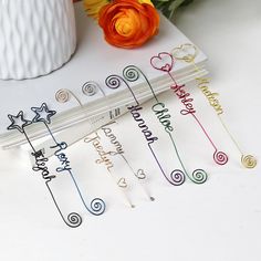 several different colored paper clips on top of a white table next to a vase with flowers