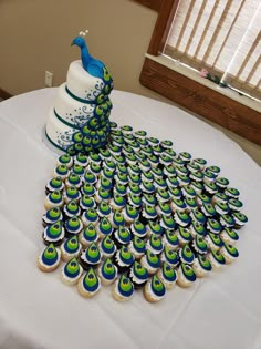 a peacock cake and cupcakes on a white tablecloth with windows in the background