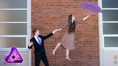 a man and woman jumping up in the air with an umbrella over their heads on a brick wall