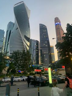 people are walking on the sidewalk in front of some very tall buildings at dusk time