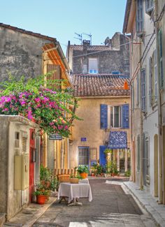 an alleyway with tables and flowers in the middle of it, surrounded by buildings