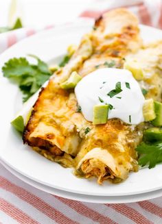 an enchilada on a plate with sour cream and cilantro garnish