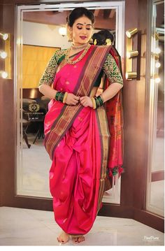 a woman in a pink sari and gold jewelry standing by a door with her hands on her hips