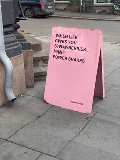 a pink sign sitting on the side of a road next to a street light and stairs