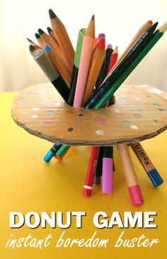 a wooden holder filled with colored pencils on top of a yellow table next to the words donut game instant boredom buster